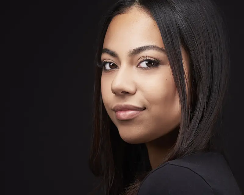 Young actress in black on black outfit against dark backdrop for acting headshot in Phoenix showing black wardrobe done right