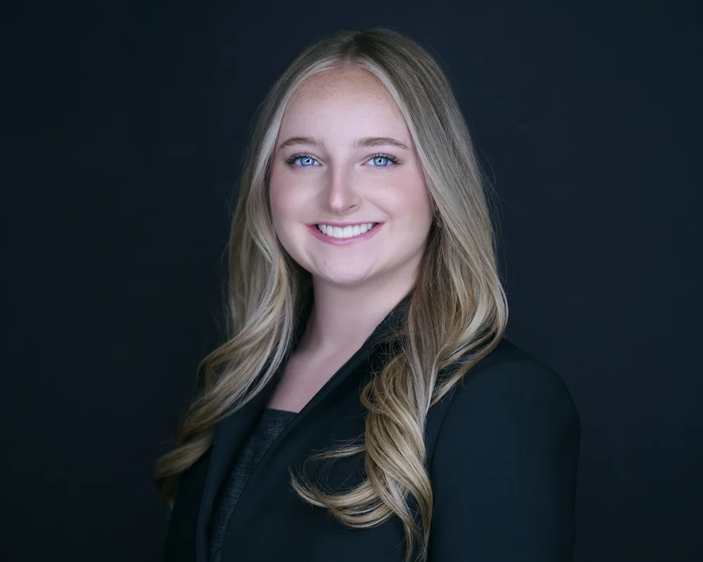 Sydney Schutz, actor portrait with long blonde hair and bright smile against dark backdrop by Marie Feutrier