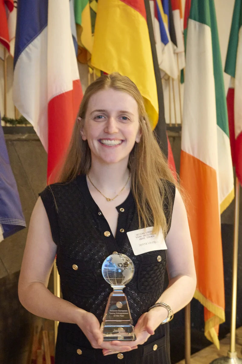 Jenna Leurquin founder and CEO of JL Patisserie holding globe trophy as first recipient of Arizona-European Young Entrepreneur Award with European flags in background Phoenix event photography