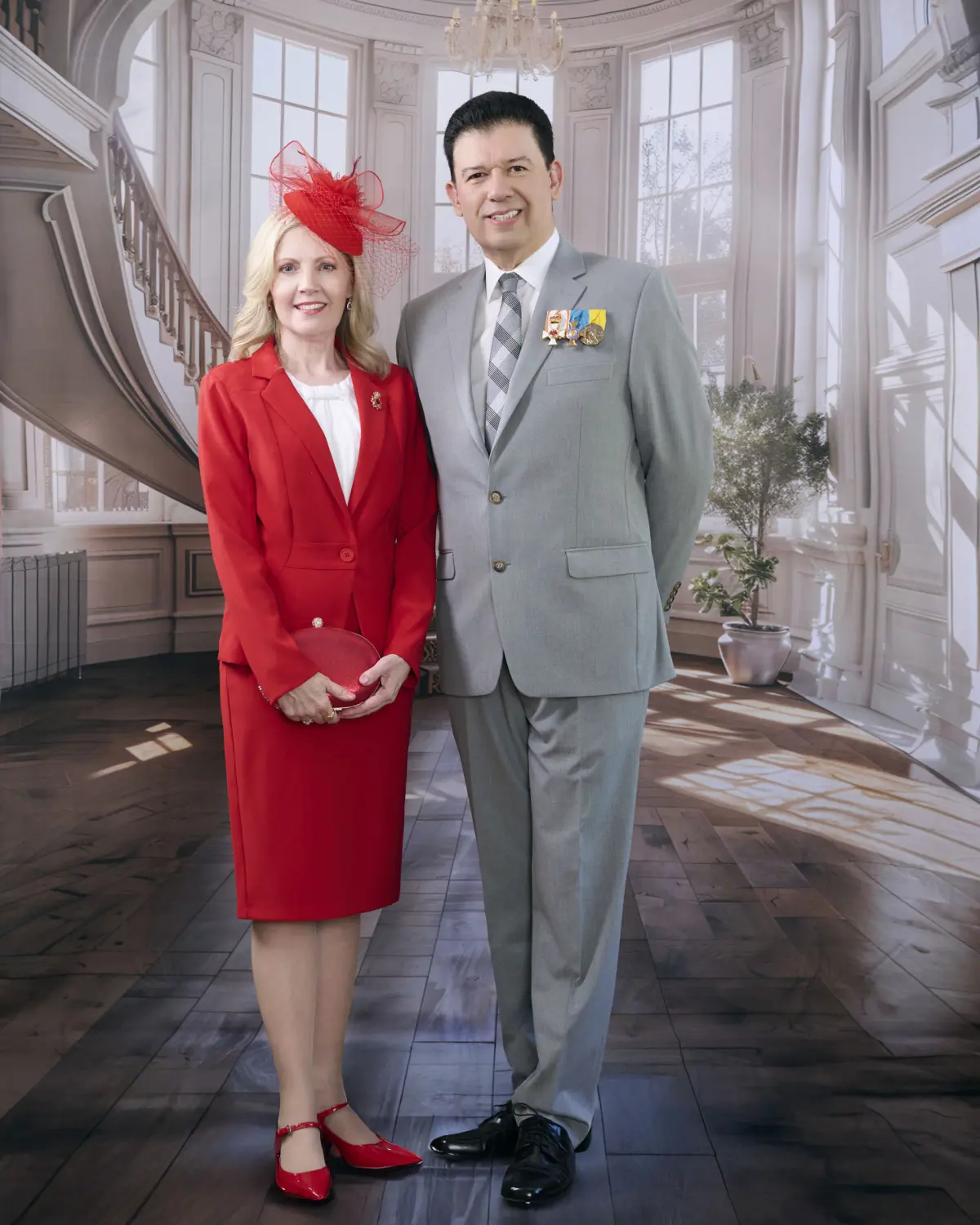 Baron in grey suit with medals and baroness in elegant red skirt suit with matching red fascinator hat, standing in front of grand mansion backdrop with curved staircase, chandelier, and tall windows with natural daylight
