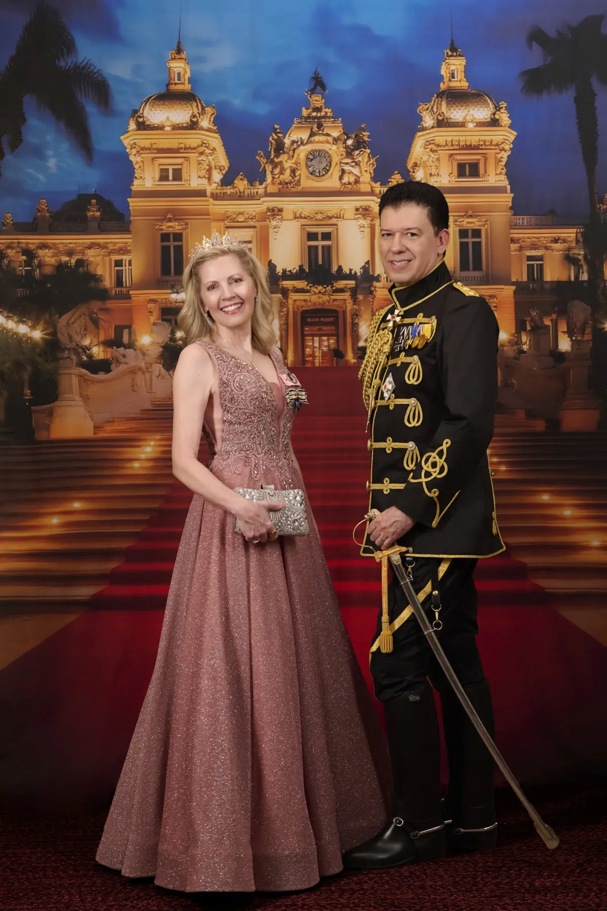 Baron in black military uniform with gold embroidery and baroness in elegant rose pink sparkle ball gown with tiara, standing in front of Monte Carlo Casino backdrop with red carpet stairs, warm golden hour lighting matching the evening casino scene