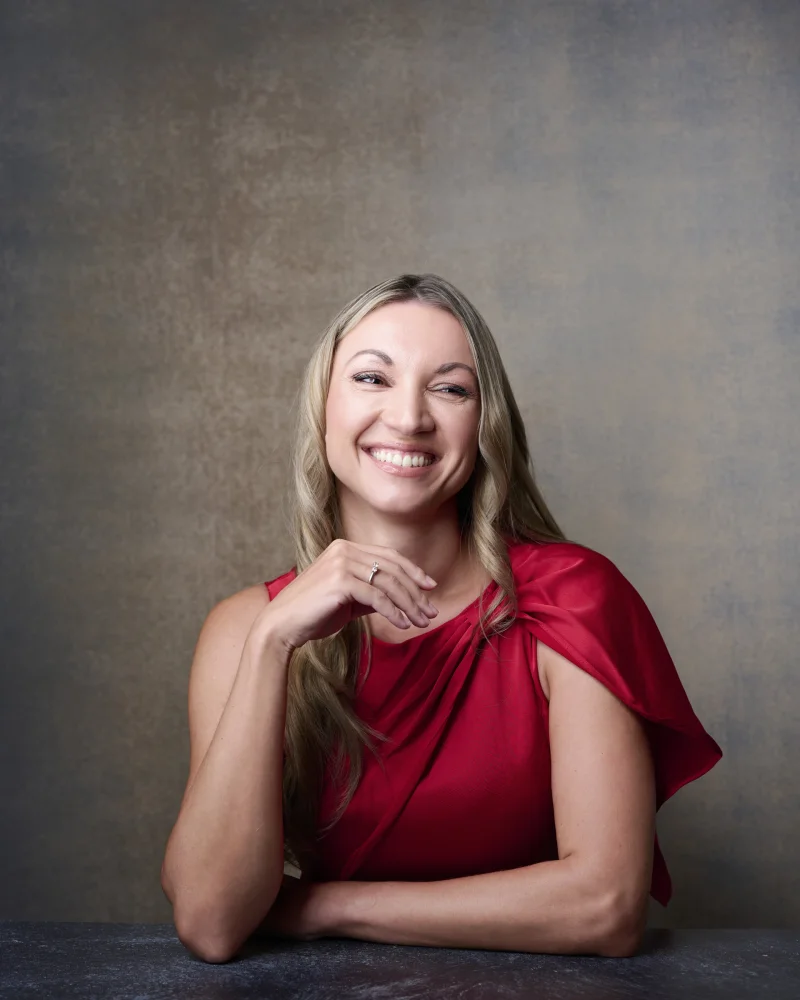 Professional headshot of a woman with natural makeup, satin lips, and a warm smile in a red top photographed in Phoenix studio