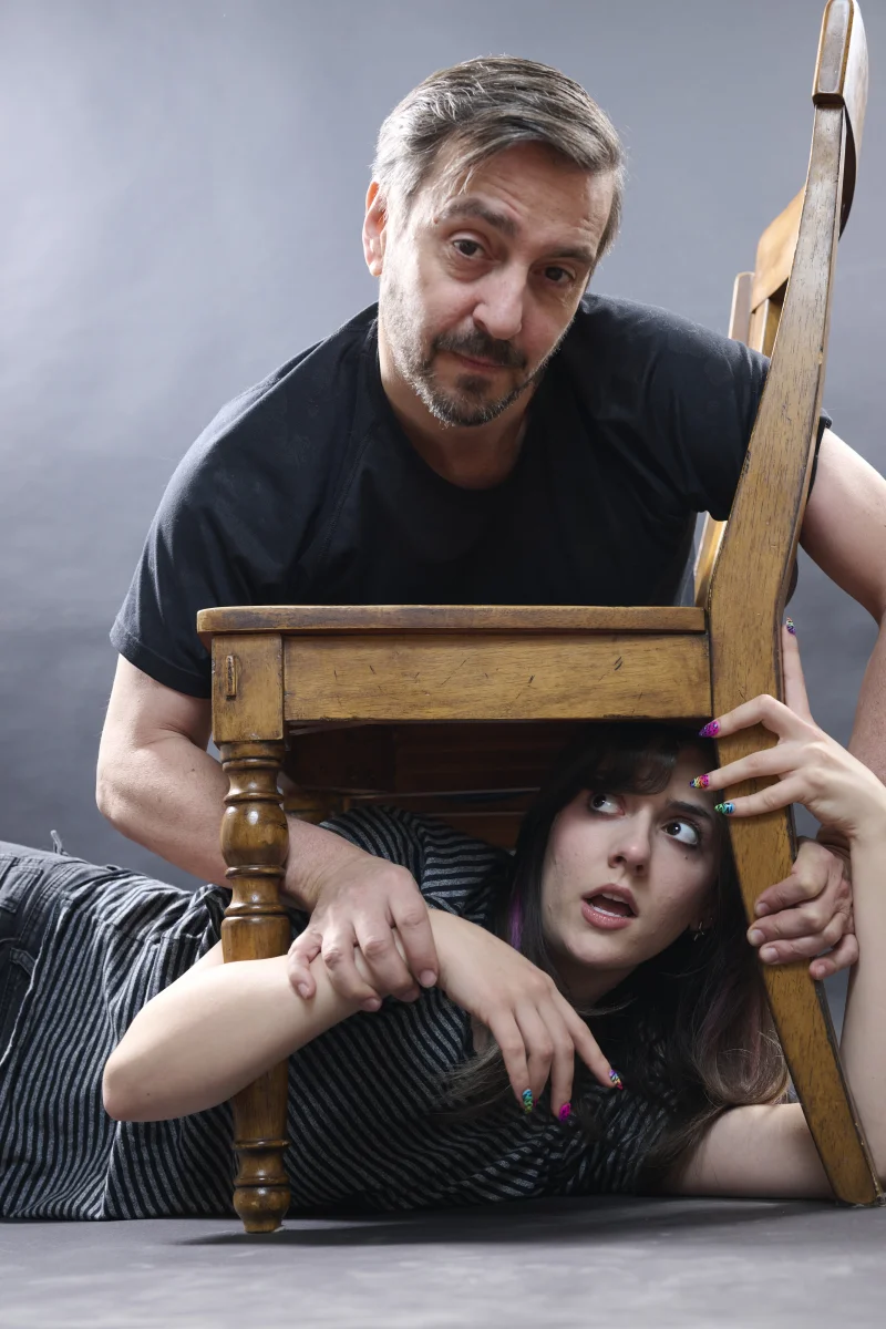 Conceptual portrait of a man and young woman with arms weaving through a wooden chair, creating spatial complexity that challenges AI image generation
