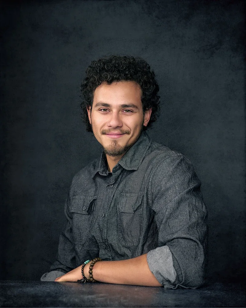 Young man in a grey button-down shirt with rolled sleeves smiling for a relaxed professional headshot