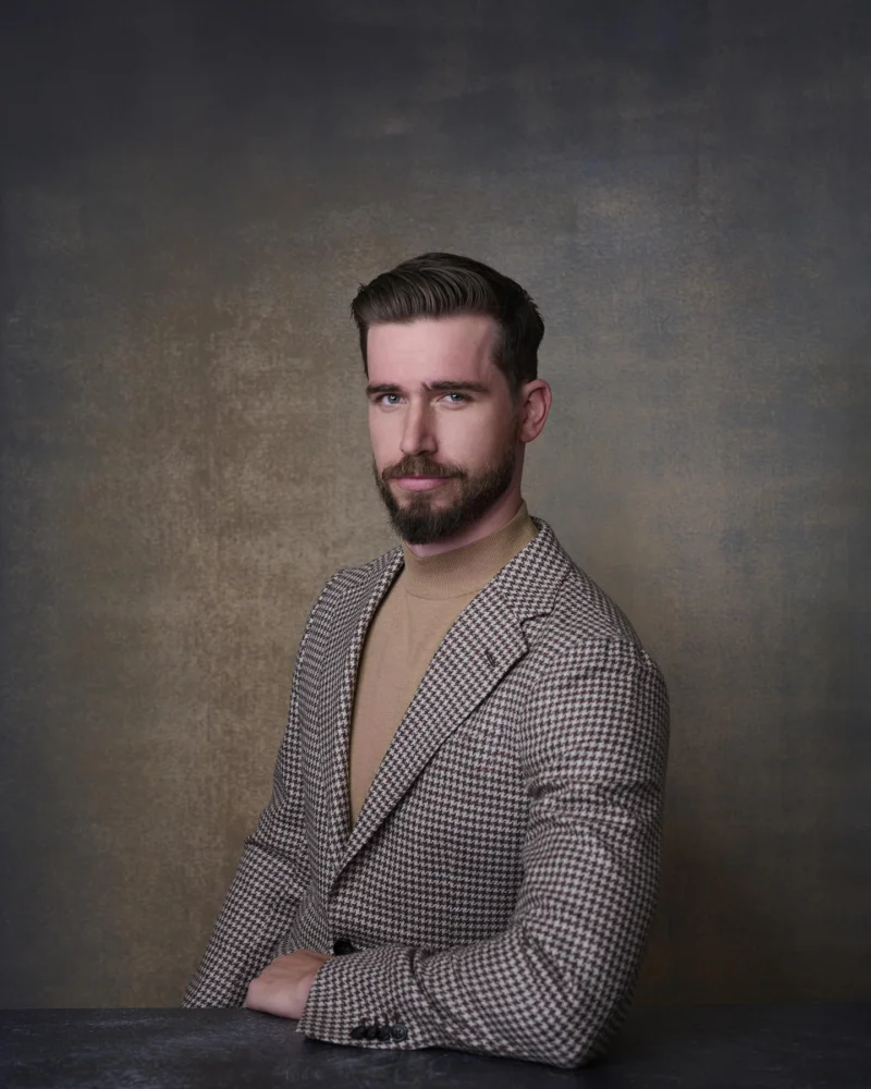 Man in a houndstooth blazer over a tan turtleneck with a well-groomed beard showing confident personal style in a professional headshot