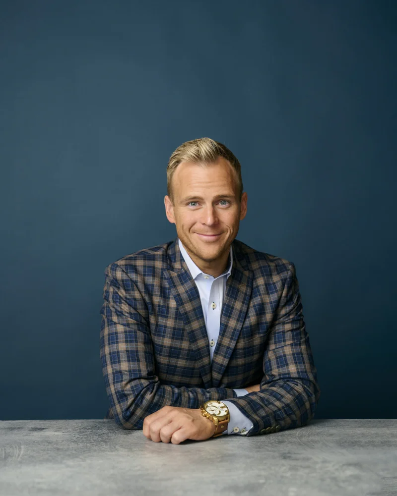 Man in a plaid blazer with a gold watch visible on his wrist during a professional headshot session