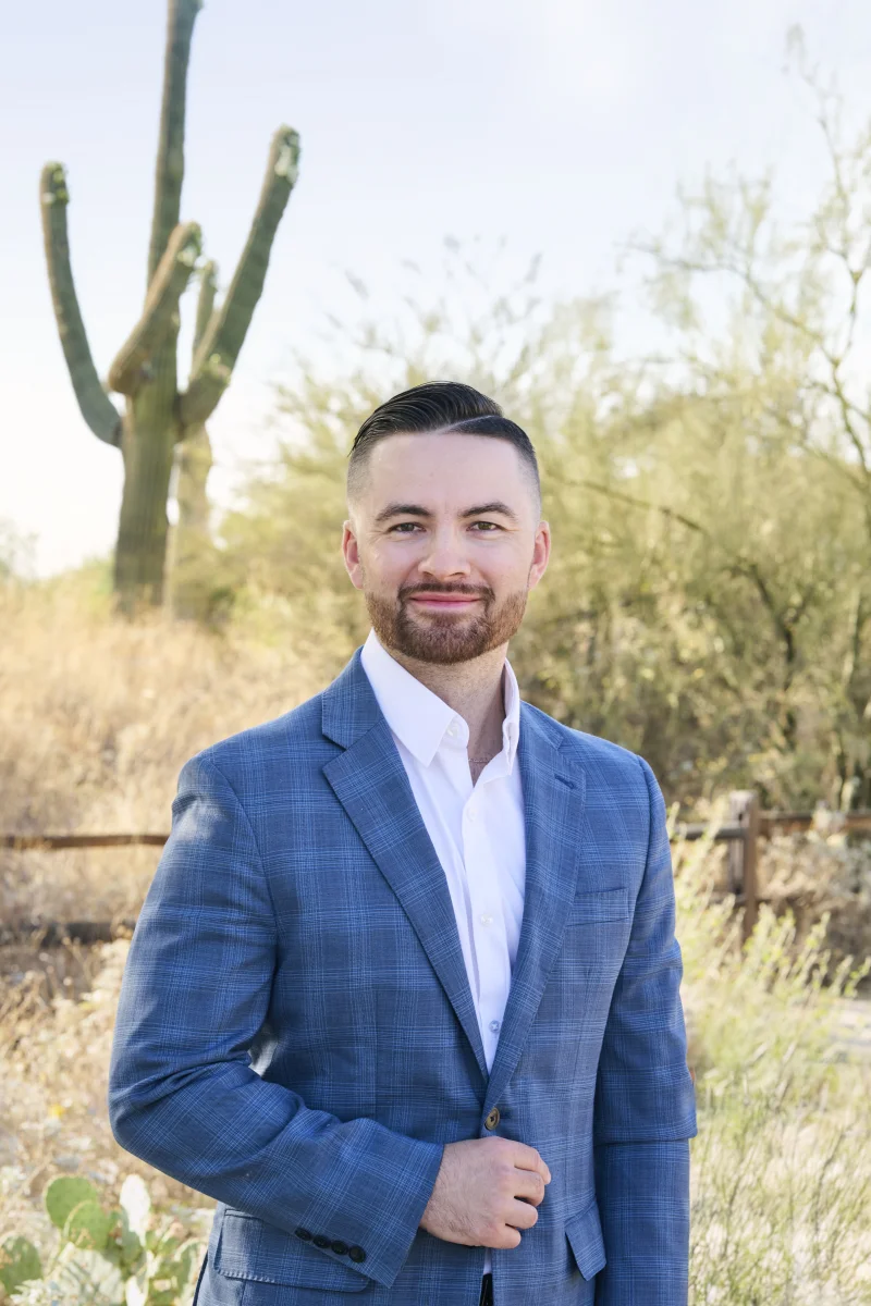 Professional outdoor headshot in Phoenix with saguaro cactus and desert landscape behind a man in a blue plaid blazer