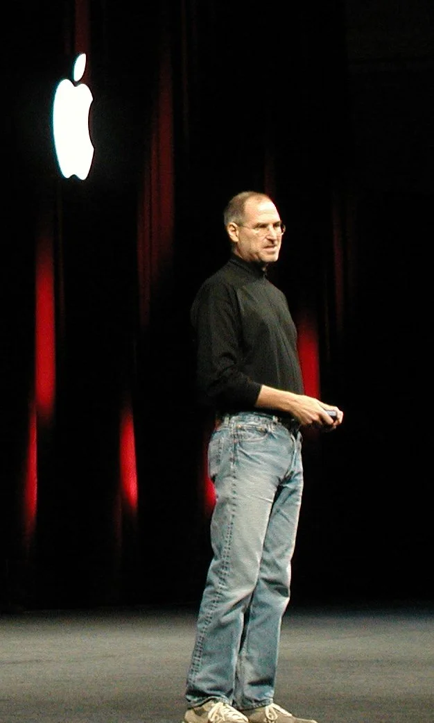 Steve Jobs presenting at Macworld 2005 in his signature black turtleneck and jeans — proof that authority doesn't require a suit