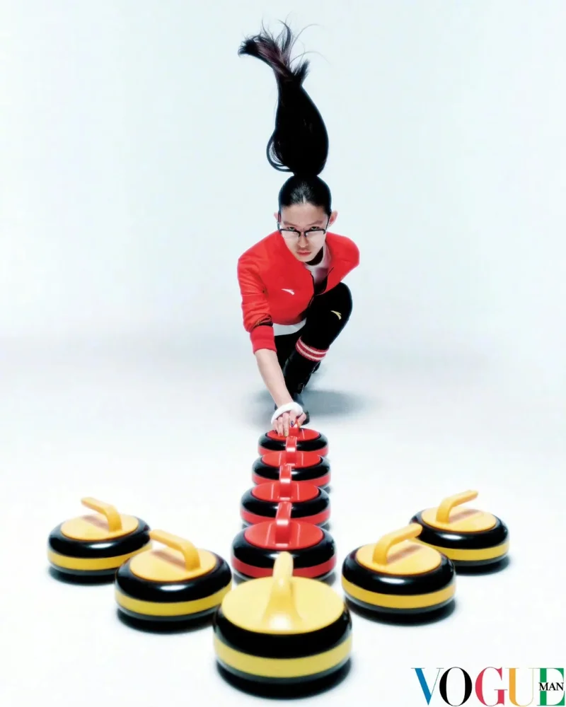 Woman in red Team China uniform crouching over stacked curling stones with her ponytail shooting straight up, photographed by Win Tam for Vogue China