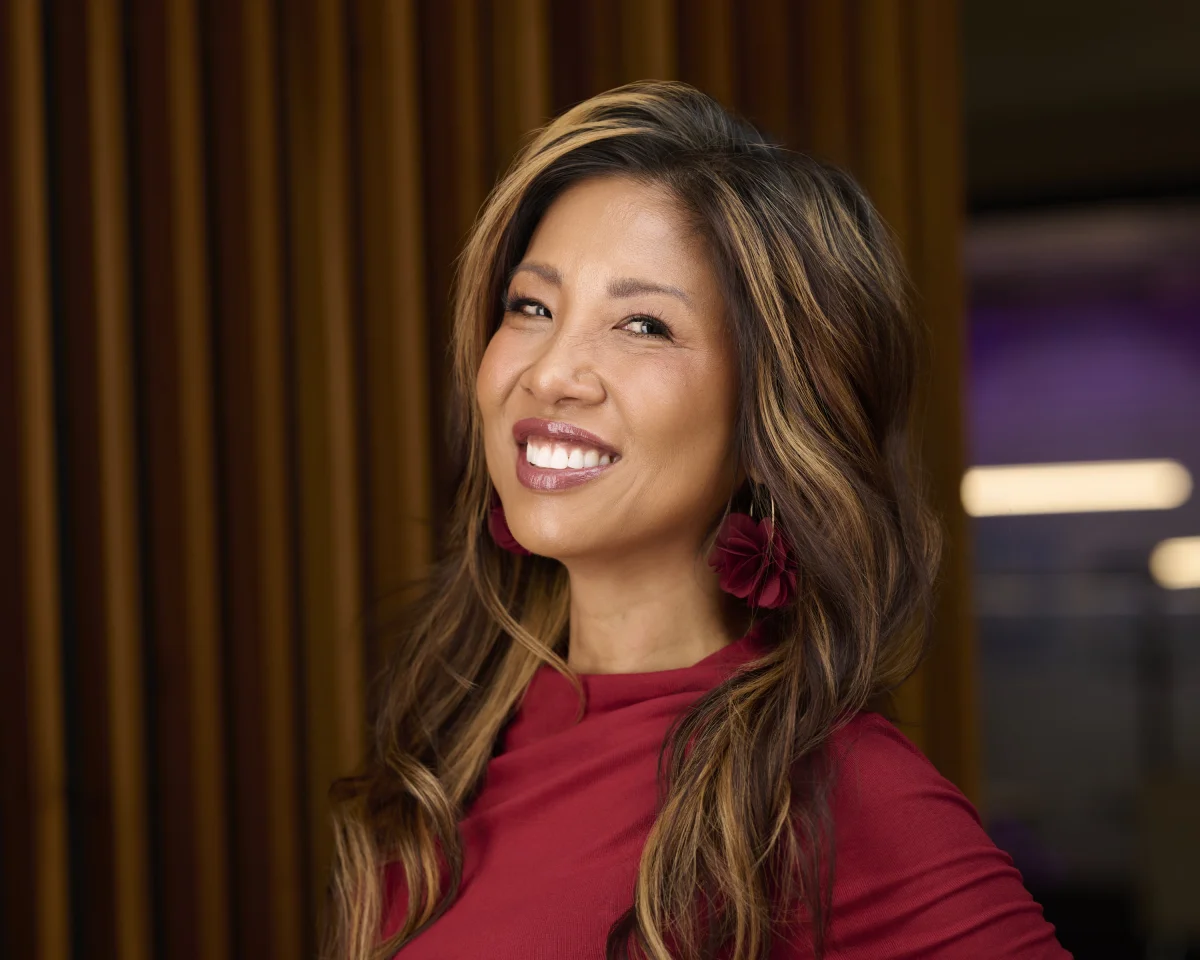 Jennifer, speaker portrait in red top with bright smile against wood slat backdrop by Marie Feutrier
