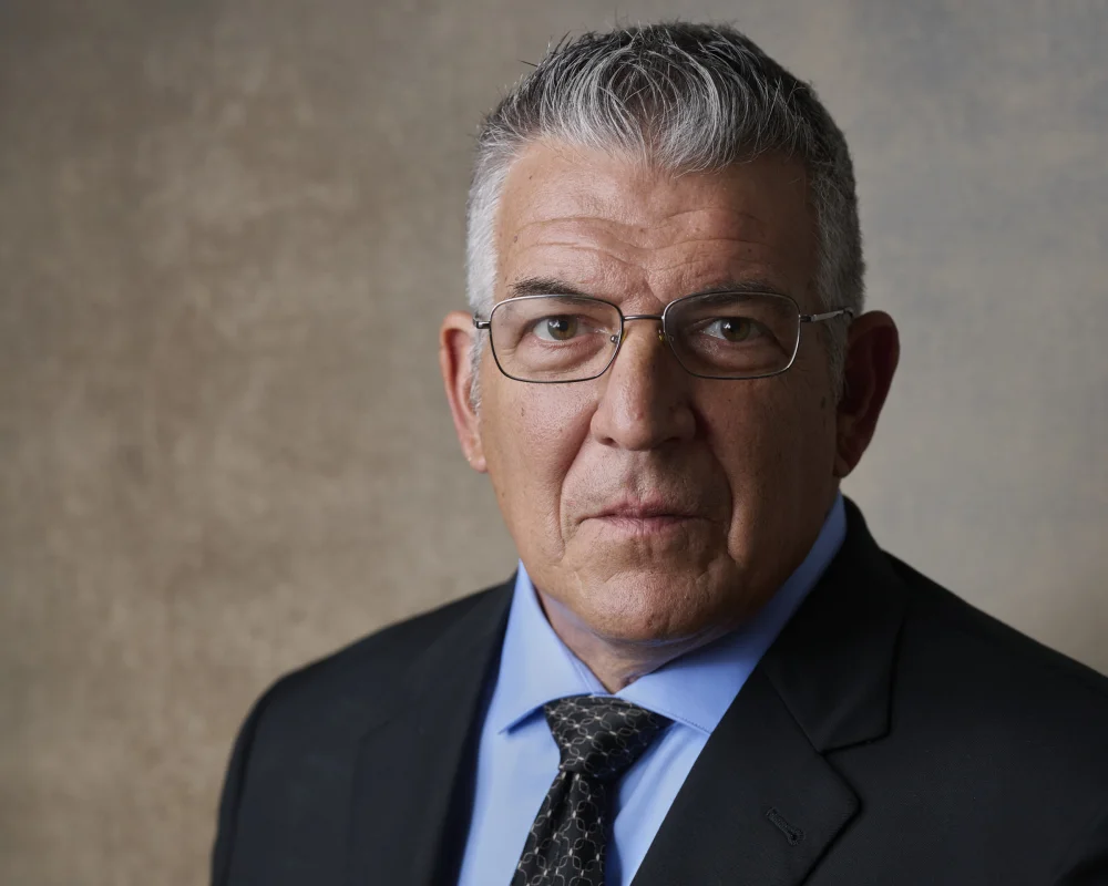 John Leligdon, executive portrait in navy suit and glasses against warm textured backdrop by Marie Feutrier