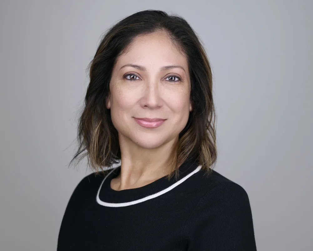Lisa Amendarez, professional portrait in black sweater with soft smile against light backdrop by Marie Feutrier