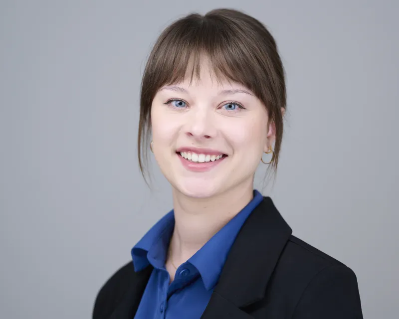 Young woman in black blazer over blue blouse with bangs and warm smile during ERAS headshot session Phoenix