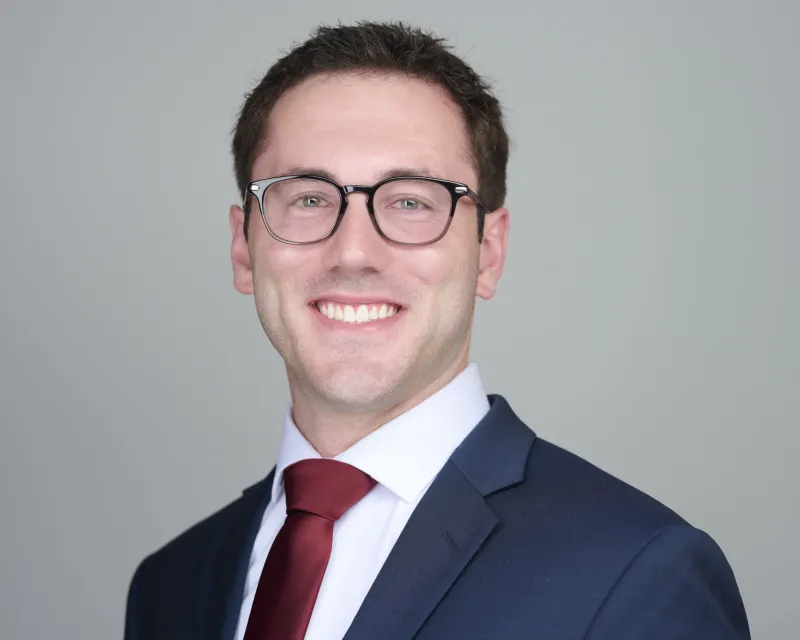 Man in navy suit with burgundy tie and glasses smiling confidently ERAS residency headshot against gray backdrop Phoenix