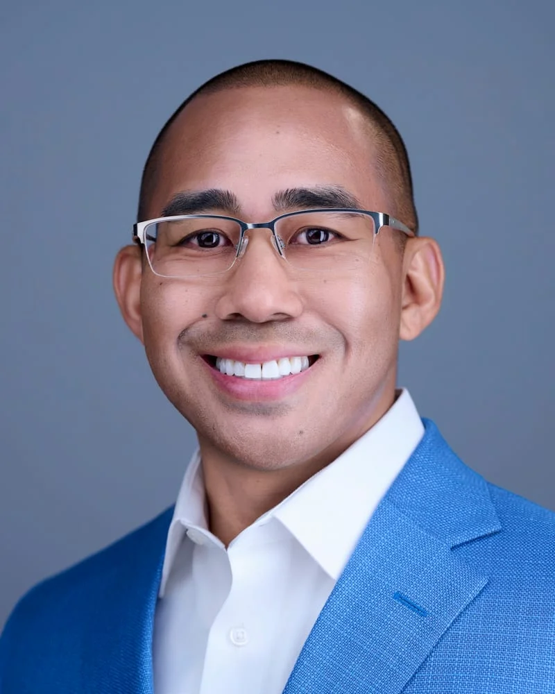 Man in bright blue blazer and white dress shirt with silver-framed glasses warm smile ERAS headshot against blue-gray backdrop Phoenix
