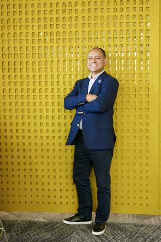 Stefano McGhee against a yellow patterned wall, arms crossed
