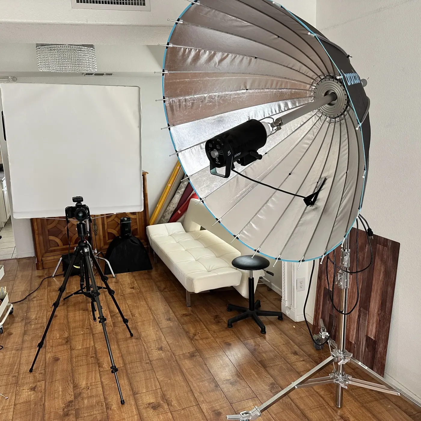 Professional photography studio setup featuring large silver parabolic umbrella modifier, white backdrop, and camera equipment